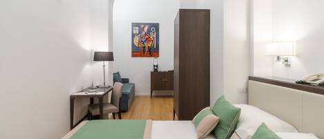 A hotel room with a bed, desk, chair, and a painting on the wall.