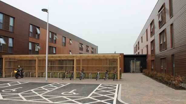 Een modern gebouw met een overdekte fietsenstalling en een parkeerplaats voor rolstoelen.