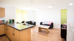 Een moderne woonkamer met een keuken, houten kastjes, een eettafel en twee banken.