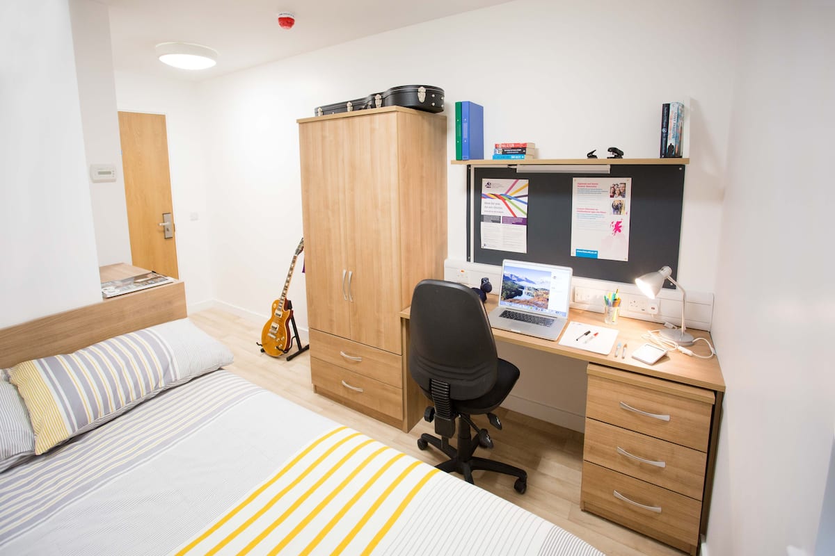 Un dormitorio con una cama, un escritorio con un ordenador, una guitarra y un armario.