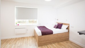 Een slaapkamer met een houten bed, witte muren, een raam en een witte radiator.