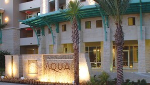 Ein Gebäude mit einer Steinfassade, einem Schild mit der Aufschrift „AQUA“ und einem überdachten Eingang mit Palmen.