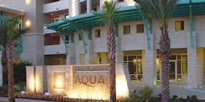A building with a stone facade, a sign reading "AQUA", and a covered entrance with palm trees. - Aqua Beach Resort by Panhandle Getaways (Panama City Beach)