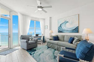Una habitación con vista al océano, un ventilador de techo, un cuadro grande de una ola y un escritorio con una lámpara.