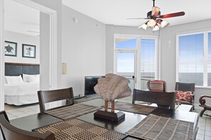 A hotel room with a bed, a dining table with chairs, a ceiling fan, and a large window with blinds. - Aqua Beach Resort by Panhandle Getaways (Panama City Beach)