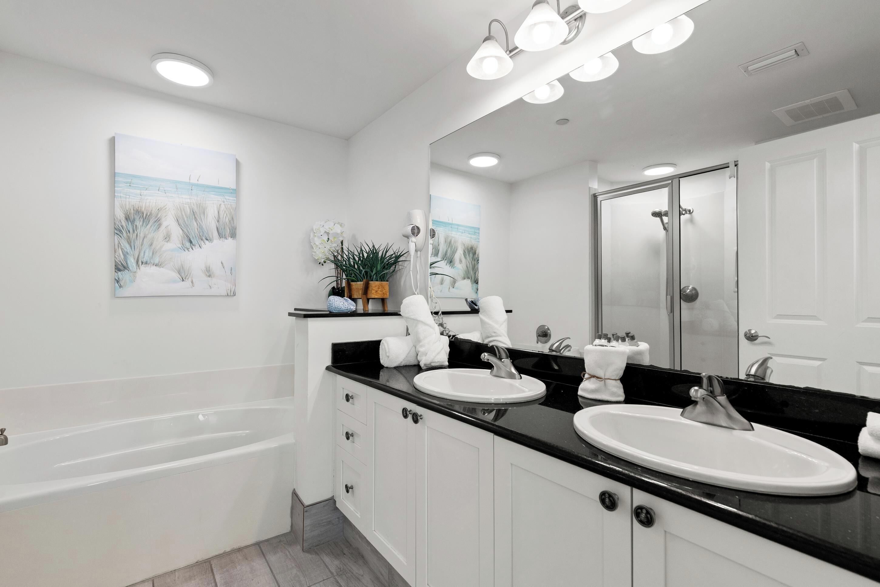 Un baño moderno con bañera, dos lavamanos, un espejo grande y luces empotradas en el techo.
