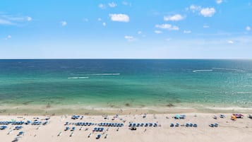 Ein Strand mit klarem, blauem Wasser, einem sandigen Ufer und mehreren Sonnenschirmen.