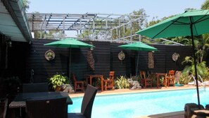 An outdoor pool area with a pergola, green umbrellas, and wooden chairs. - Country View Resort (Udon Thani)
