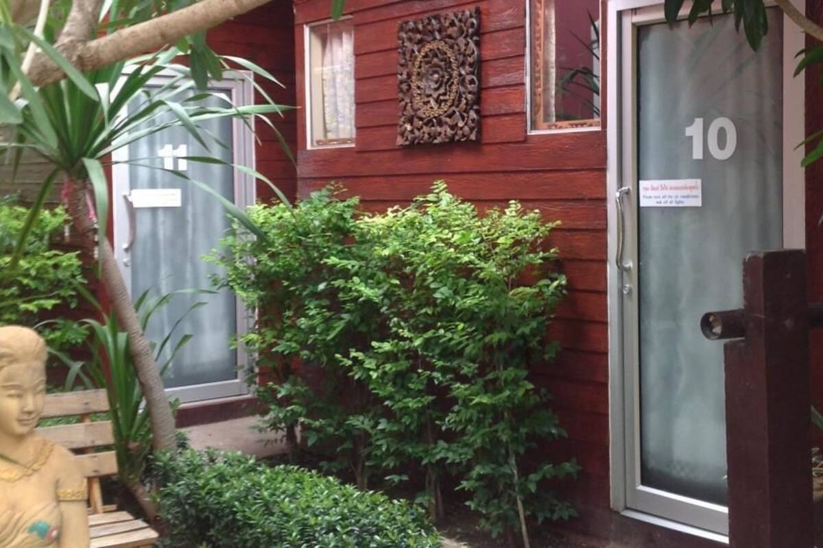 A wooden building with a door marked '10', surrounded by greenery and a small statue.