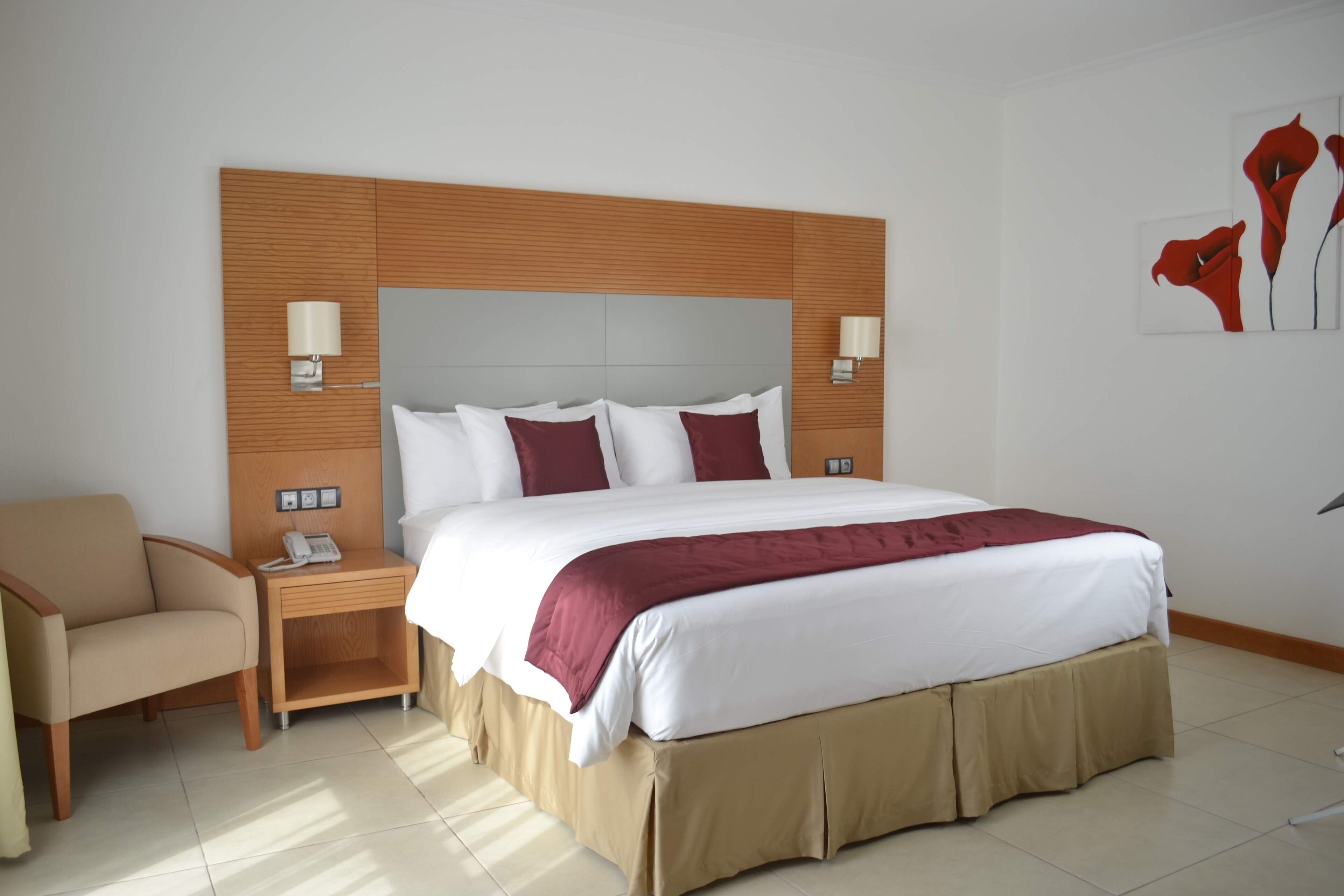Een hotelkamer met een groot bed, een nachtkastje met een lamp, een stoel en een telefoon.