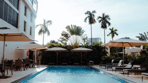 A swimming pool with lounge chairs and umbrellas, surrounded by palm trees and a building. - Star Land Hotel Bonapriso (Douala)