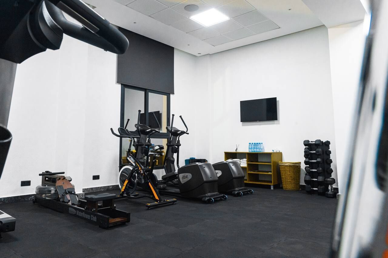 Un gimnasio con diferentes equipos de ejercicio, un dispensador de agua y un televisor en la pared.