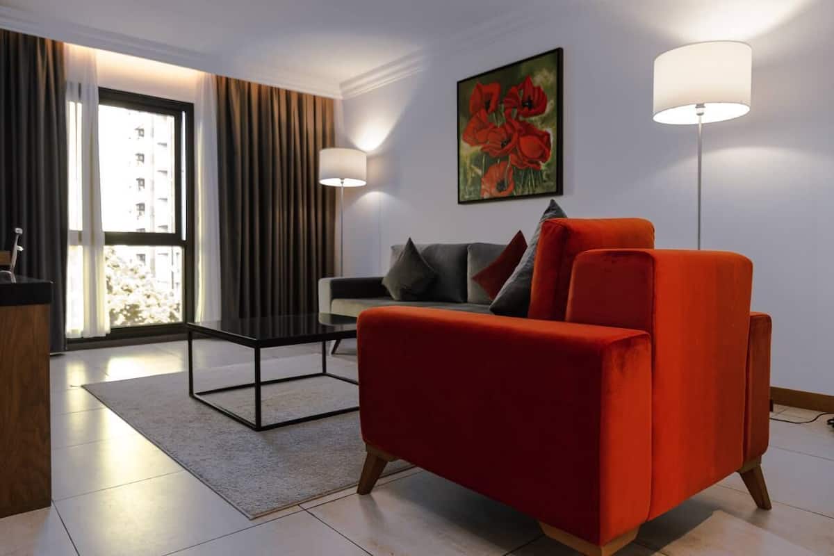 A modern living room with a red armchair, a sofa with grey cushions, a coffee table, and two floor lamps.