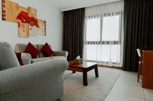 A living room with a grey sofa, red cushions, a wooden coffee table, and a painting on the wall.
