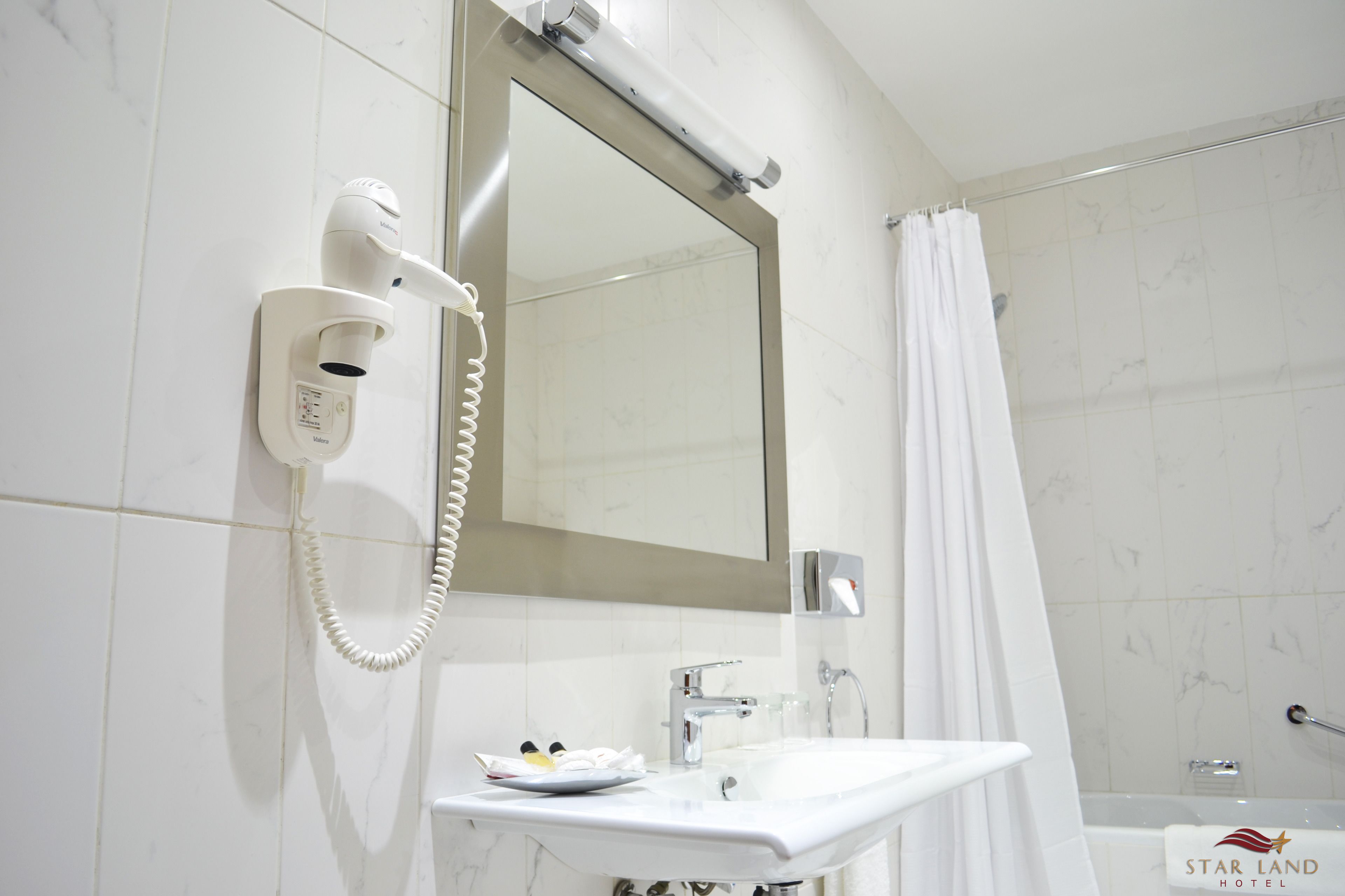 A bathroom with a white sink, a mirror, a hairdryer, and a shower curtain.