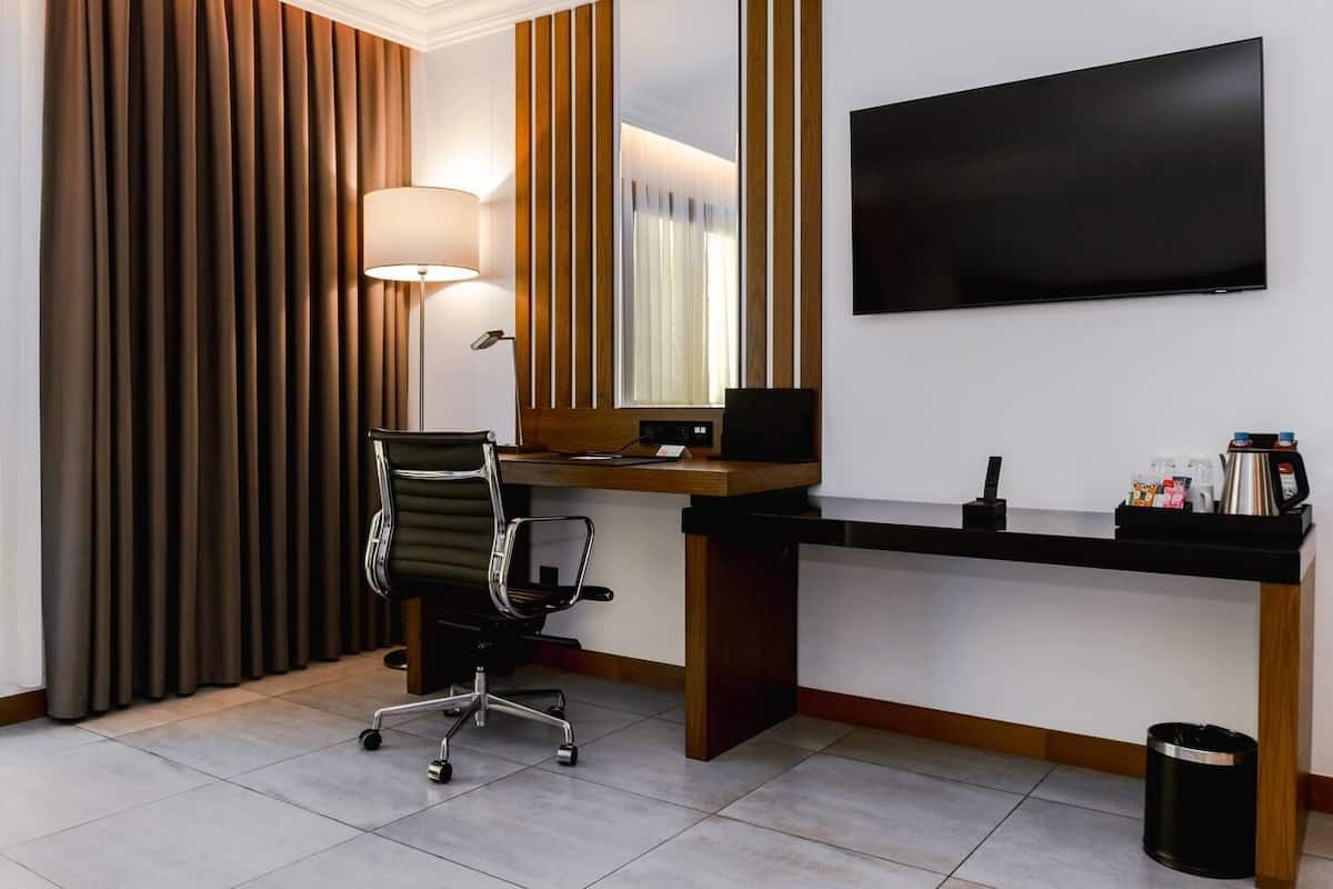 A hotel room with a desk, chair, TV, and curtains.