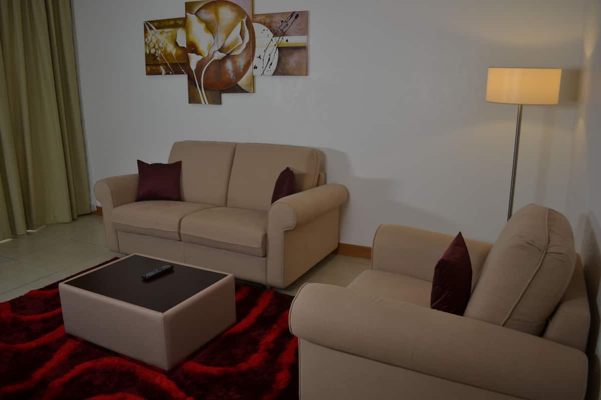A living room with a beige sofa, a matching armchair, a red rug, a coffee table, and a floor lamp.