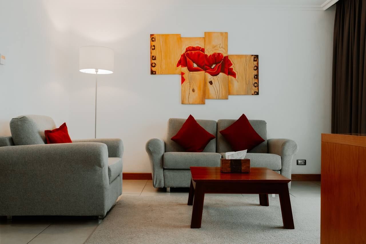 Una sala de estar moderna con dos sofás grises, cojines rojos, una mesa de centro de madera y una lámpara de pie.