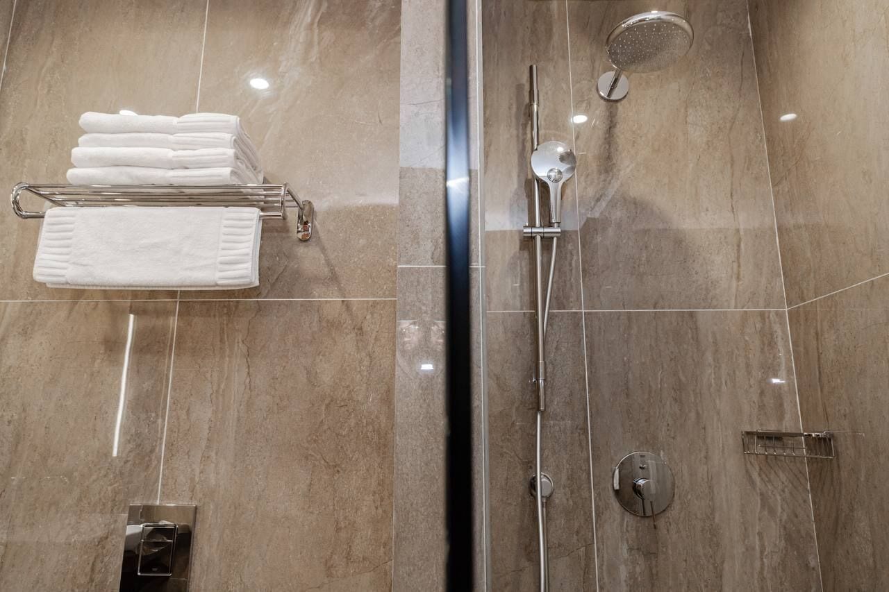 Un baño moderno con ducha de vidrio, un perchero con toallas dobladas y un panel de control en la pared.