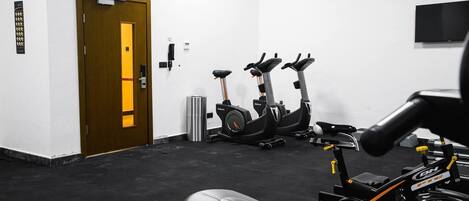 A gym with stationary bikes, a treadmill, and a door with an emergency exit sign.