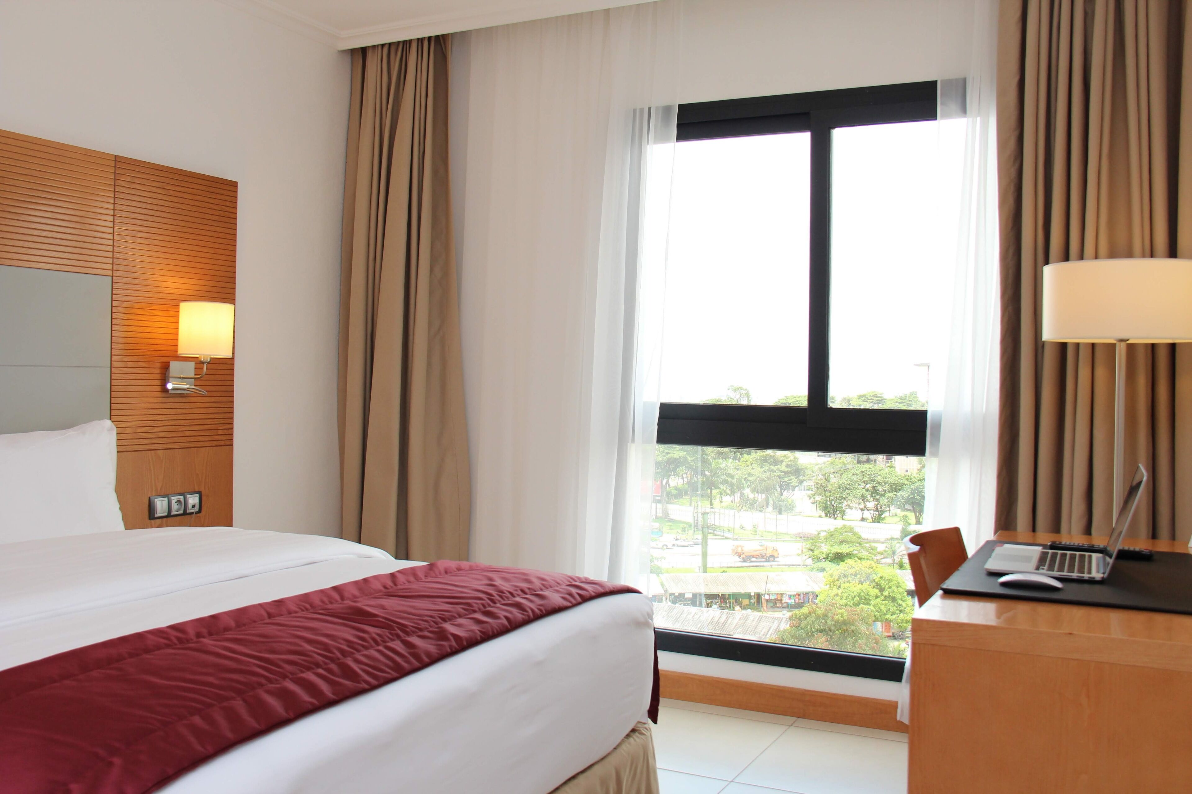 A hotel room with a large bed, a desk with a laptop, and a window with a view of the outside.