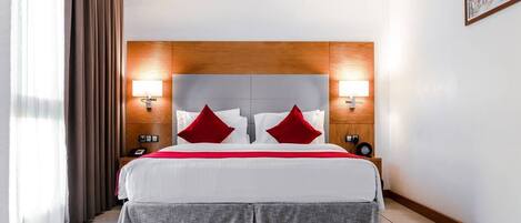 Una habitación de hotel con una cama grande, dos lámparas de noche, un cabecero de madera y una mesita de noche con un teléfono.