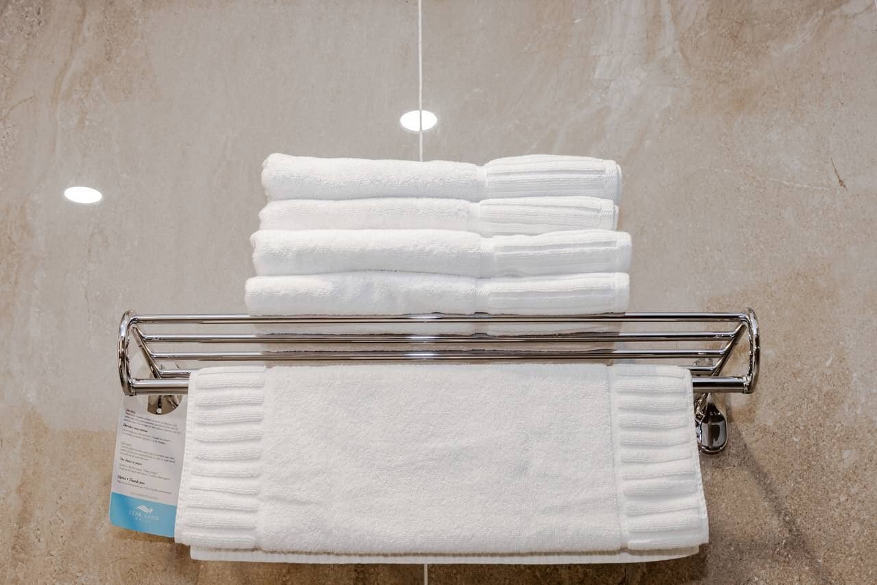 A stack of white towels on a metal towel rack against a tiled wall.
