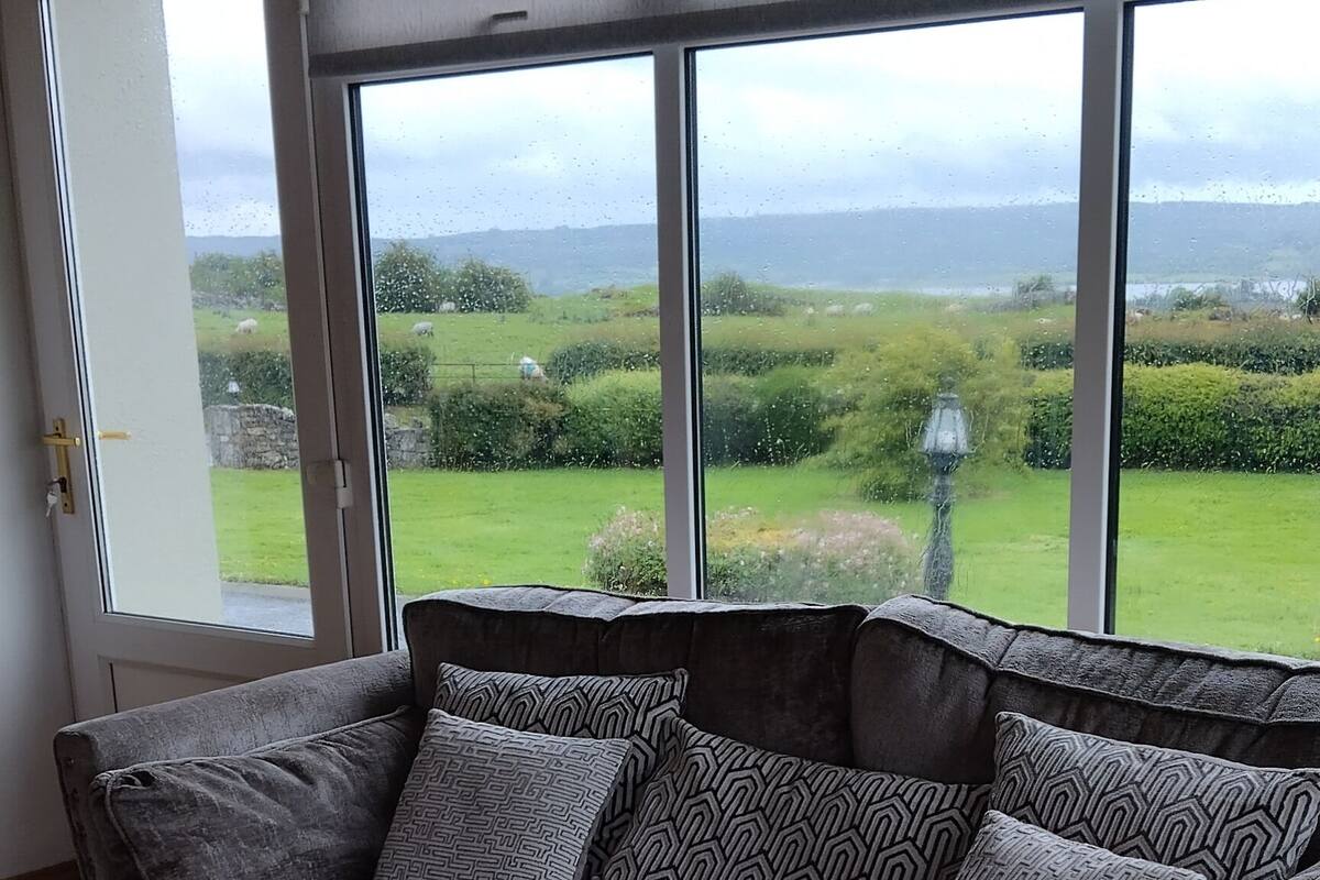 A grey sofa with patterned cushions in a room with wooden flooring and large windows.