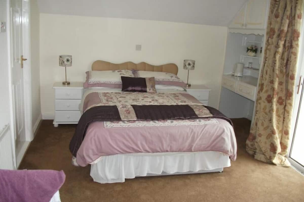 A bedroom with a bed, two bedside tables, a nightstand, a dresser, a mirror, and a window with curtains.