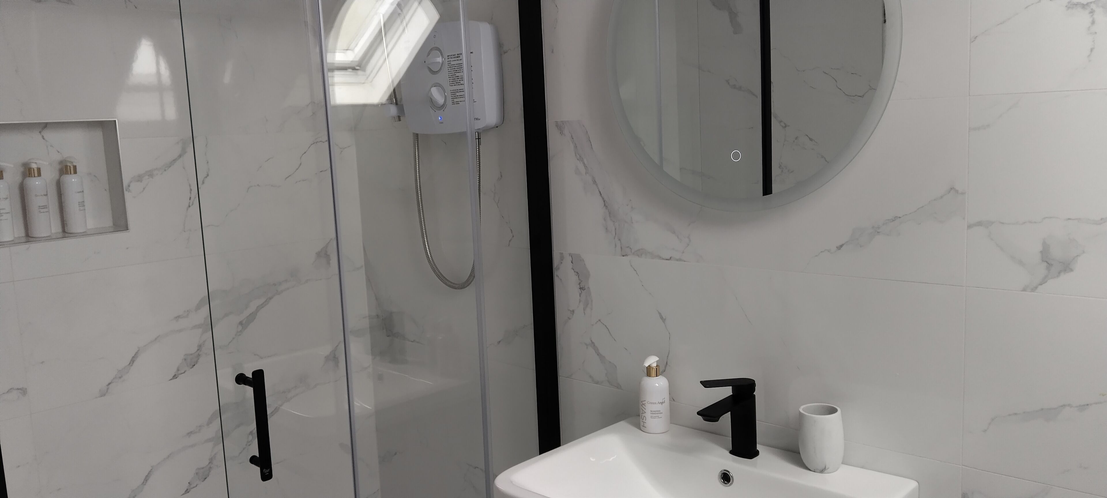 A modern bathroom with a glass shower enclosure, a white sink with a black faucet, and a mirror above the sink.