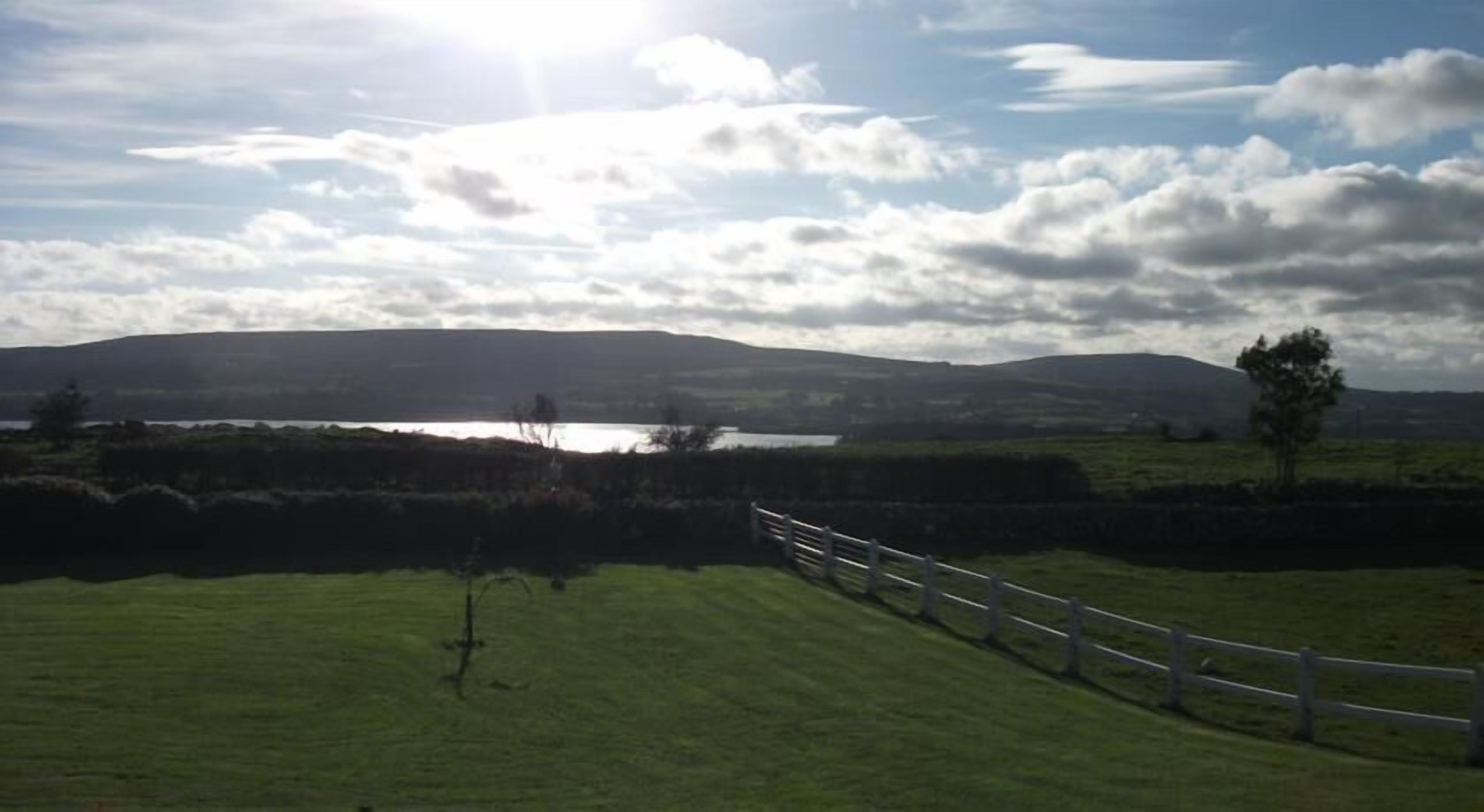 A rural landscape with a grassy field, a wooden fence, and a body of water in the distance.