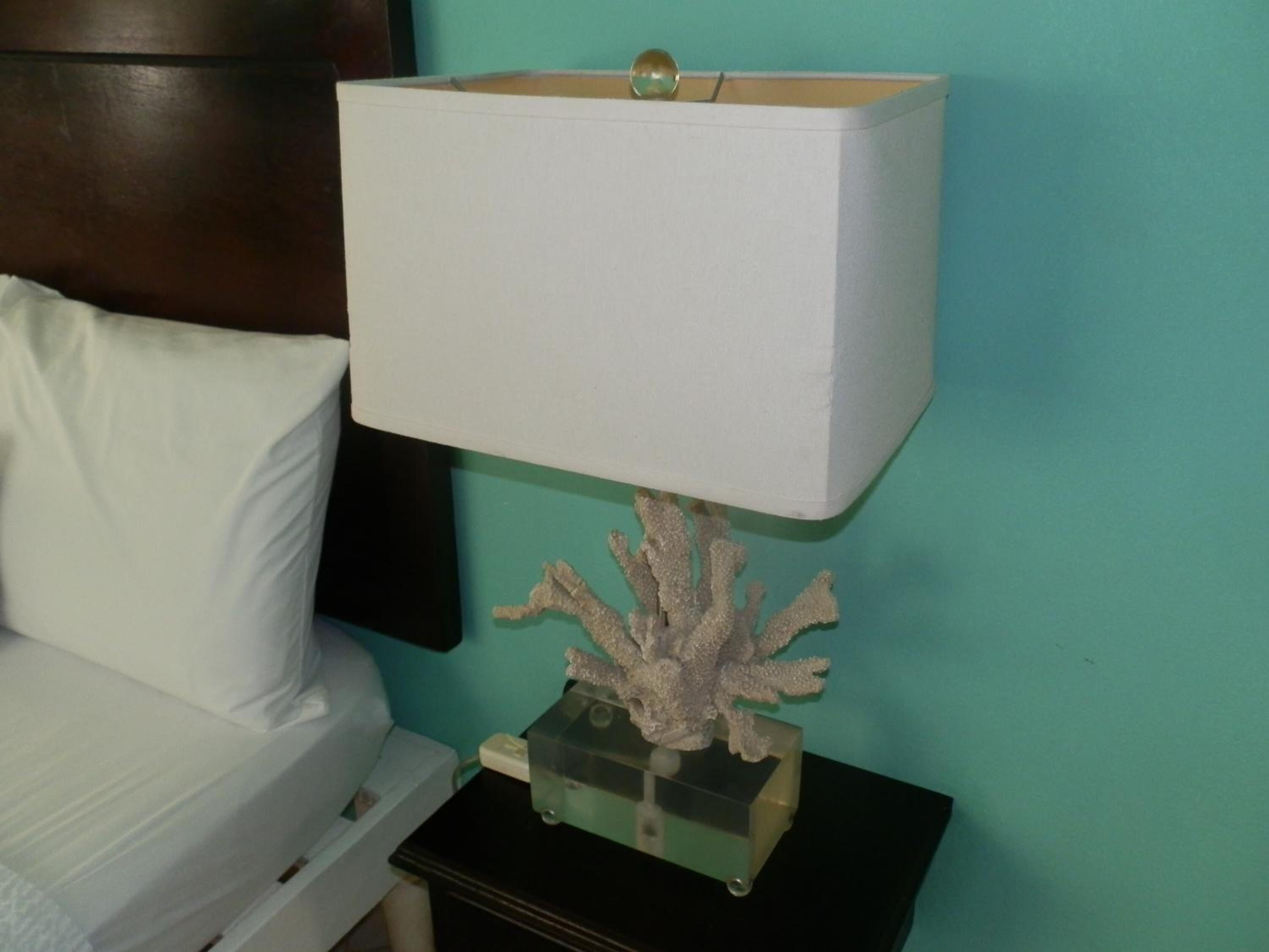 A bed with a white pillow and a nightstand with a decorative coral piece and a white lamp.