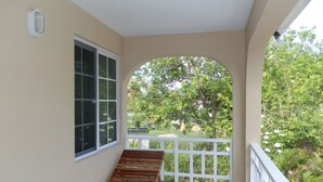 A balcony with a wooden bench, a white railing, and a view of greenery. - Paradise on the Rocks (Negril)