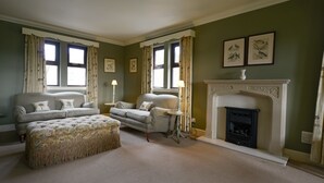 A living room with two sofas, a matching ottoman, a fireplace, and two windows with curtains. - Factors Inn & Cottage (Fort William)