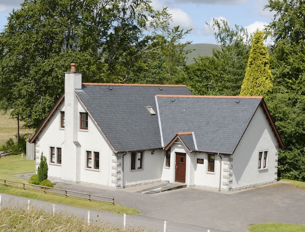 A two-story white house with a grey roof, a chimney, and a small front porch.