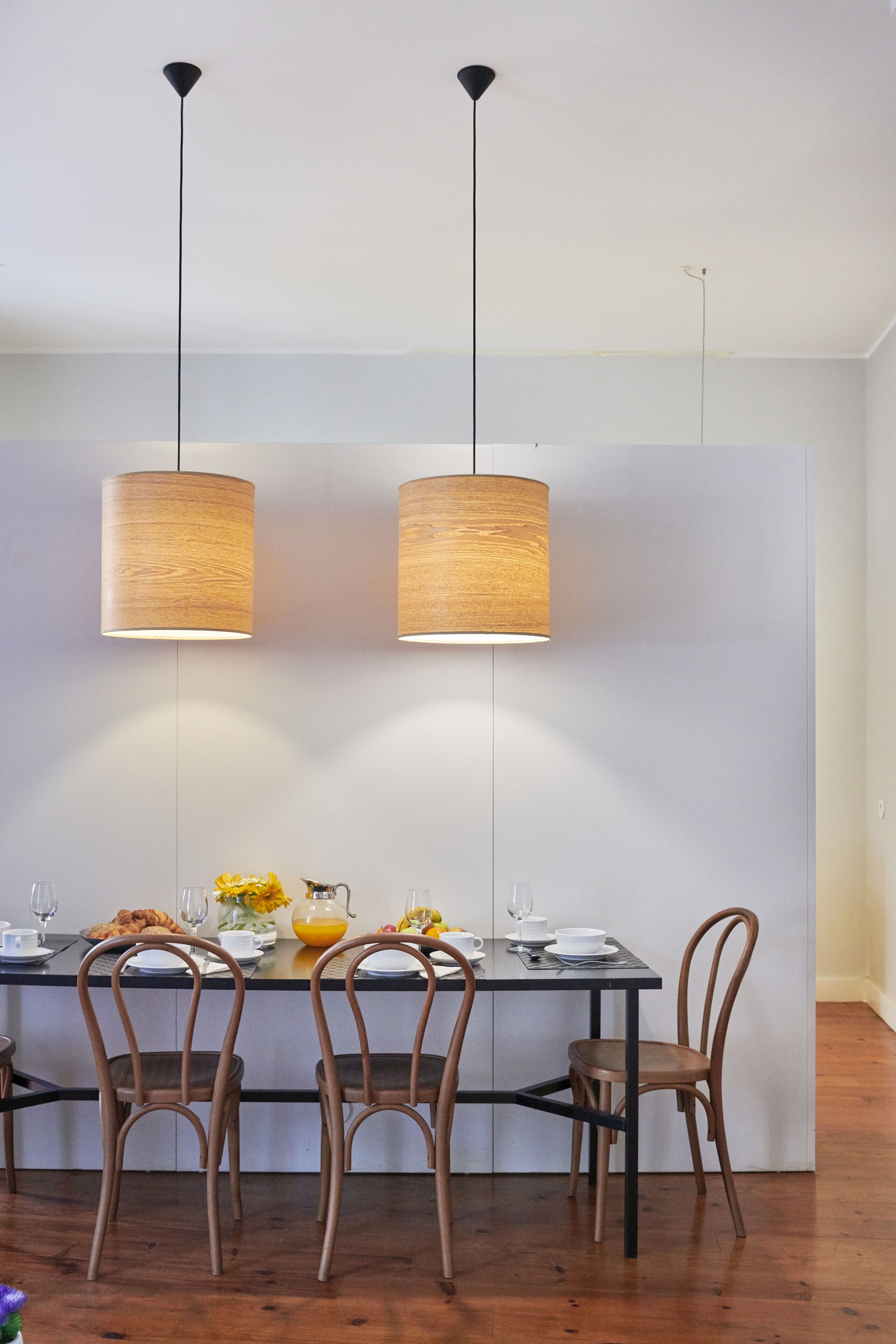 Un coin repas avec une table dressée pour quatre personnes, deux lampes suspendues et des chaises en bois.