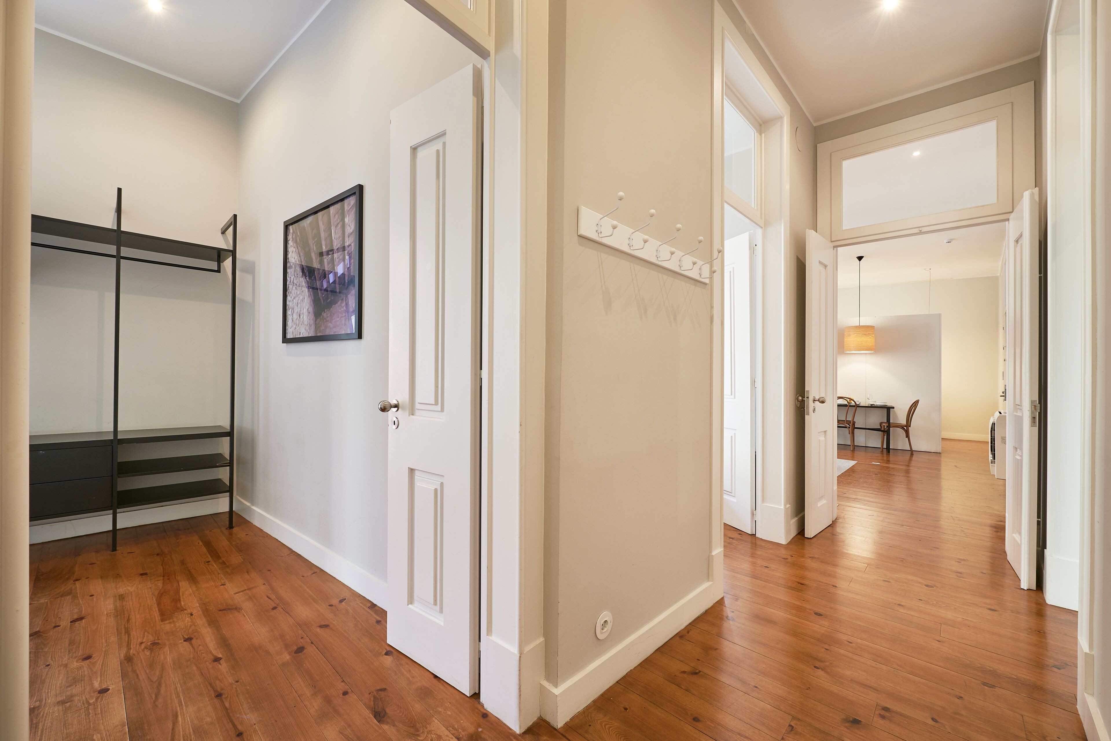 A hallway with wooden flooring, white walls, and a door leading to another room.