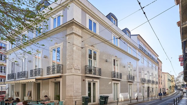 Een gebouw met een café op de begane grond, terrasjes buiten en een tramhalte in de buurt.