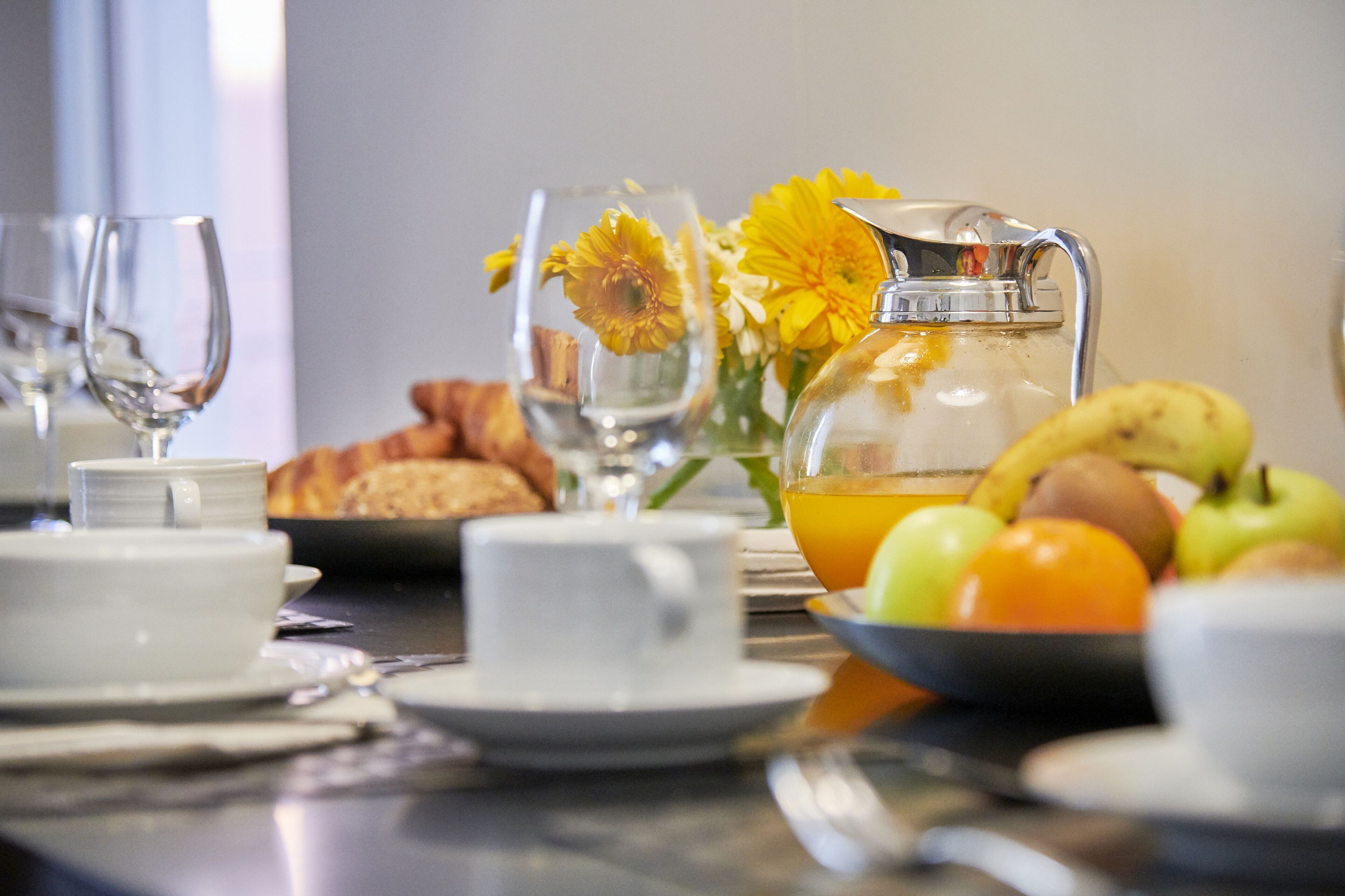 Un esmorzar amb una cafetera, un plat de fruita i pastissos damunt d'una taula.