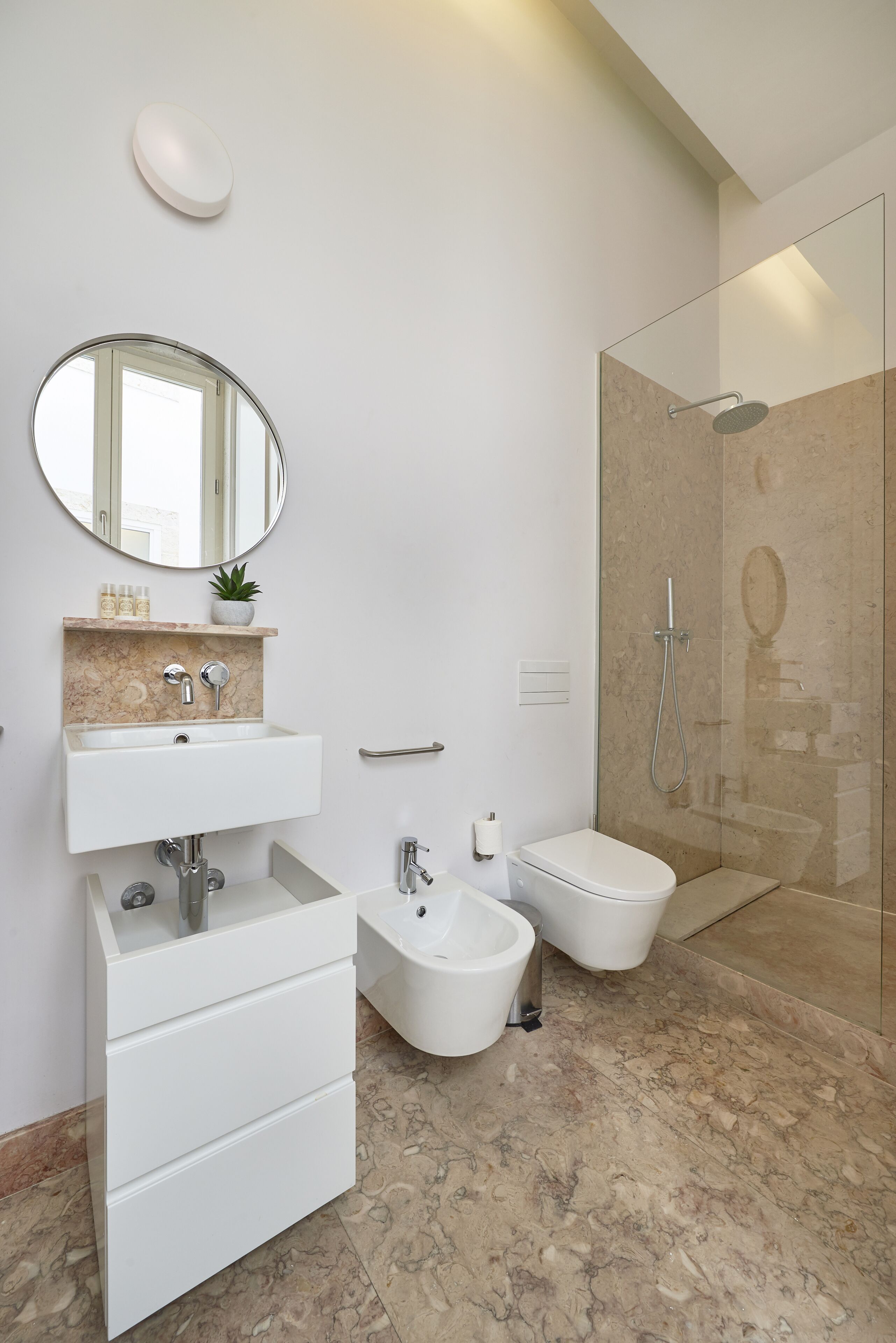 Un baño moderno con lavamanos de mármol, un bidé, una ducha con mampara de cristal y un espejo sobre el lavamanos.