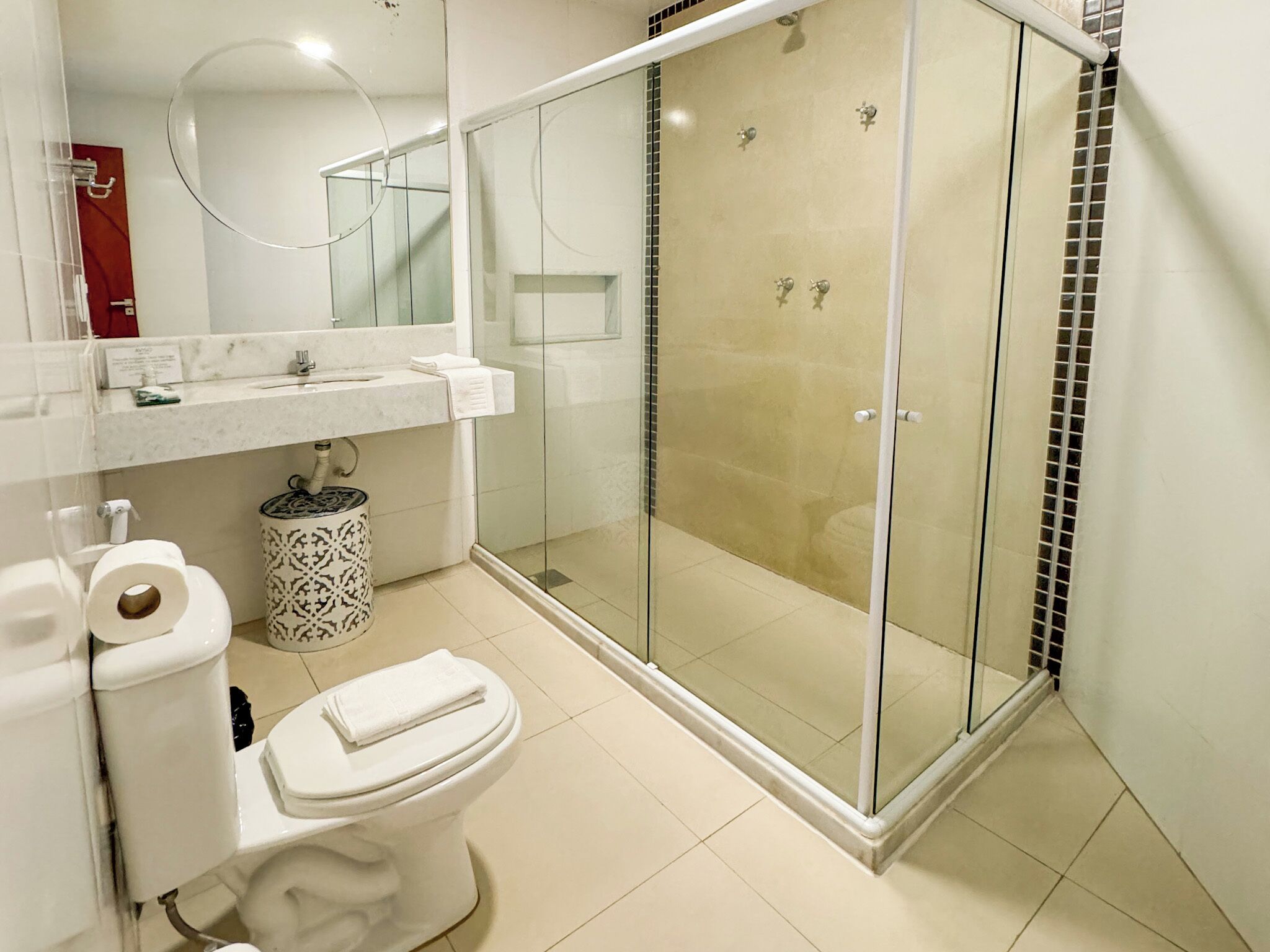 A modern bathroom with a glass-enclosed shower, a toilet, and a sink with a mirror above.