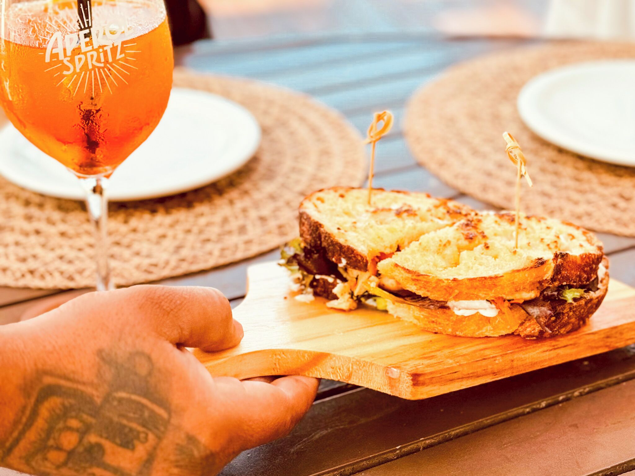 Un sándwich sobre una tabla de madera, con una bebida al frente.