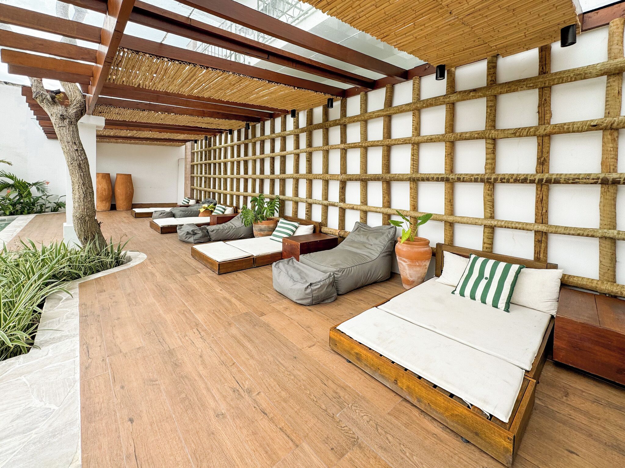 A modern outdoor lounge area with wooden flooring, multiple seating options including sofas and benches, and a bamboo wall structure.