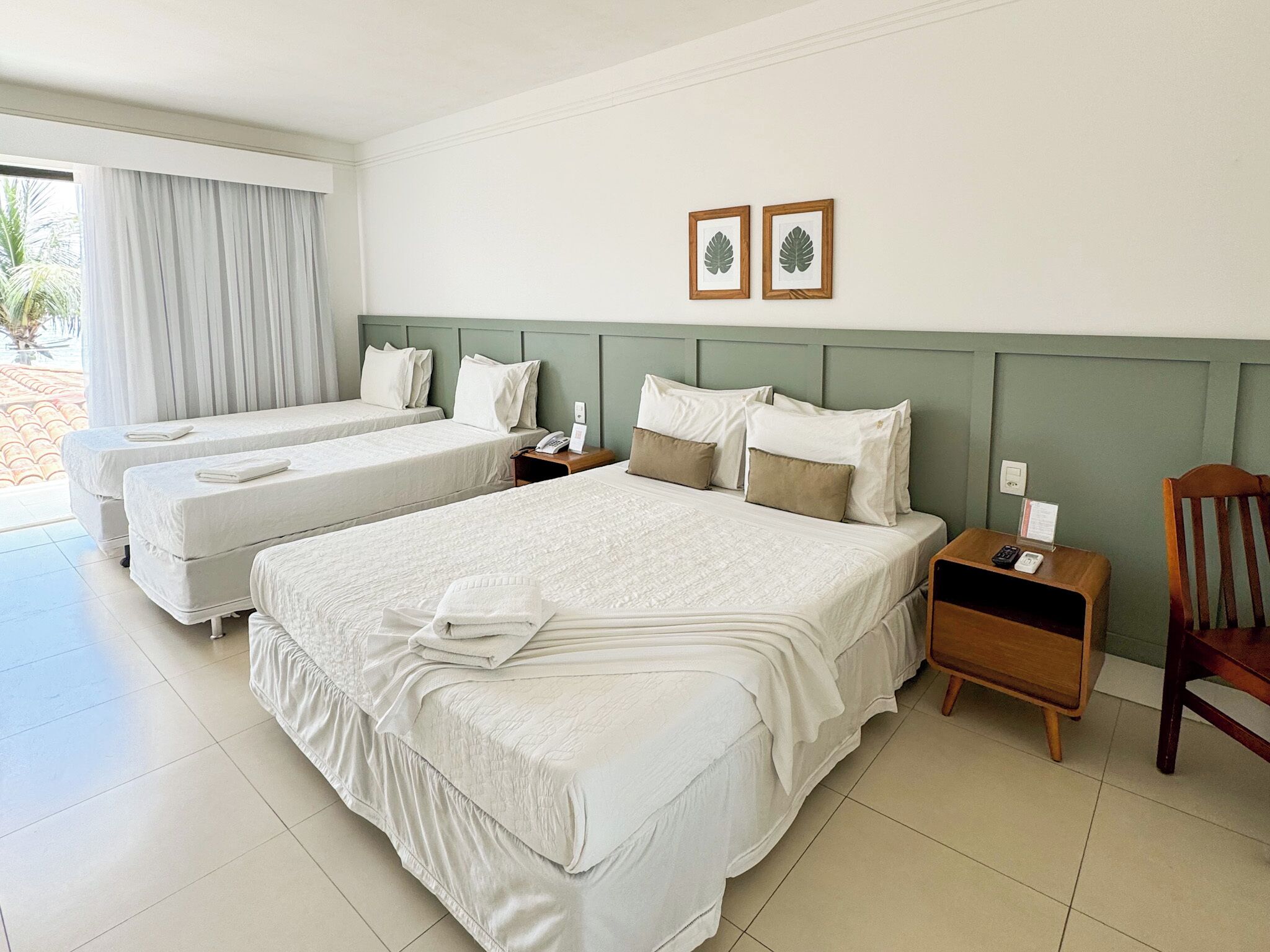 A hotel room with two beds, a wooden nightstand, a chair, and a window with curtains.