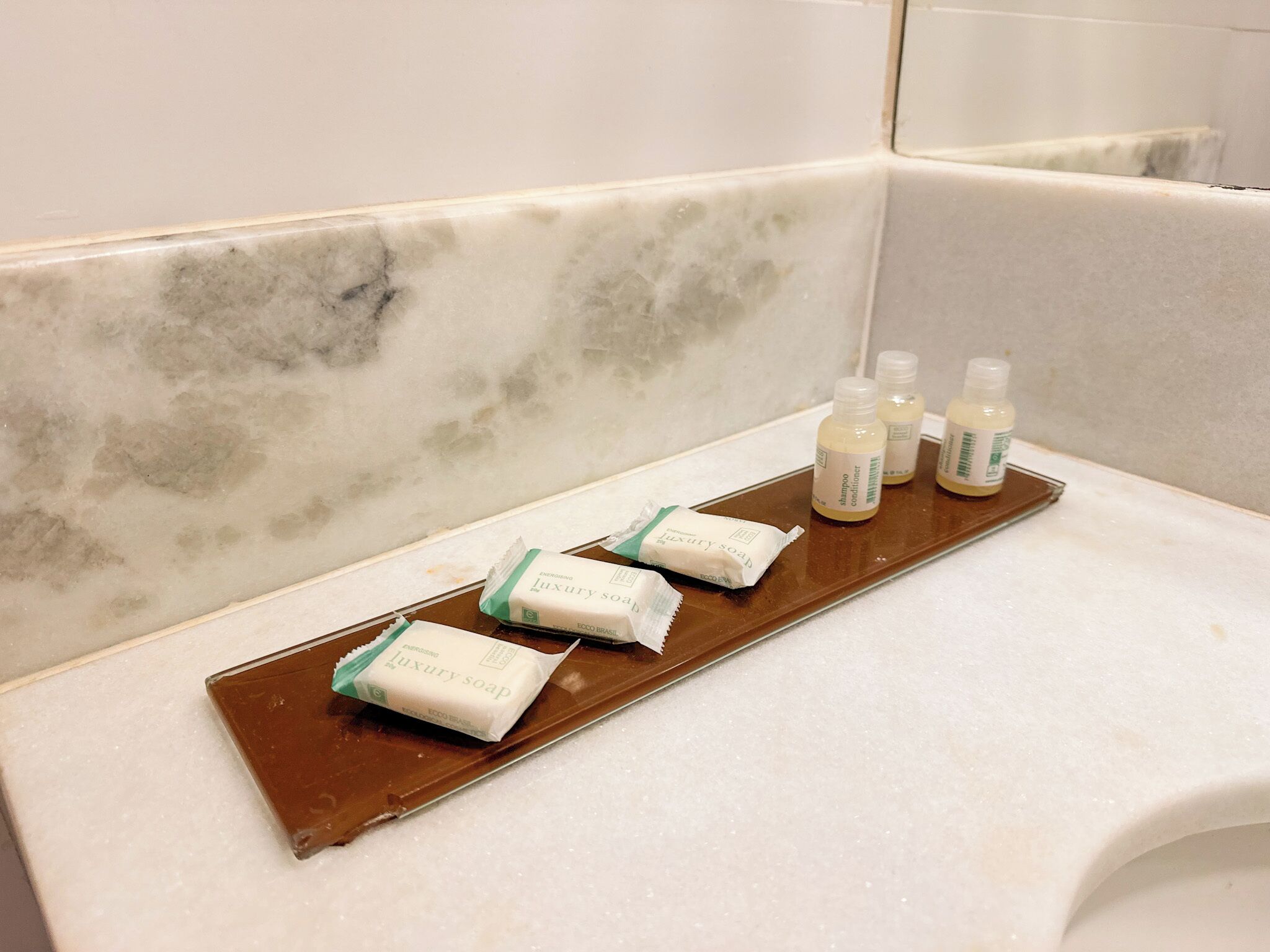 Een badkamer met een marmeren wastafel, drie flessen shampoo en conditioner, en twee luxe zeepjes op een dienblad.