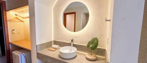 A modern bathroom with a large round mirror, a white sink, and a small plant on the vanity.
