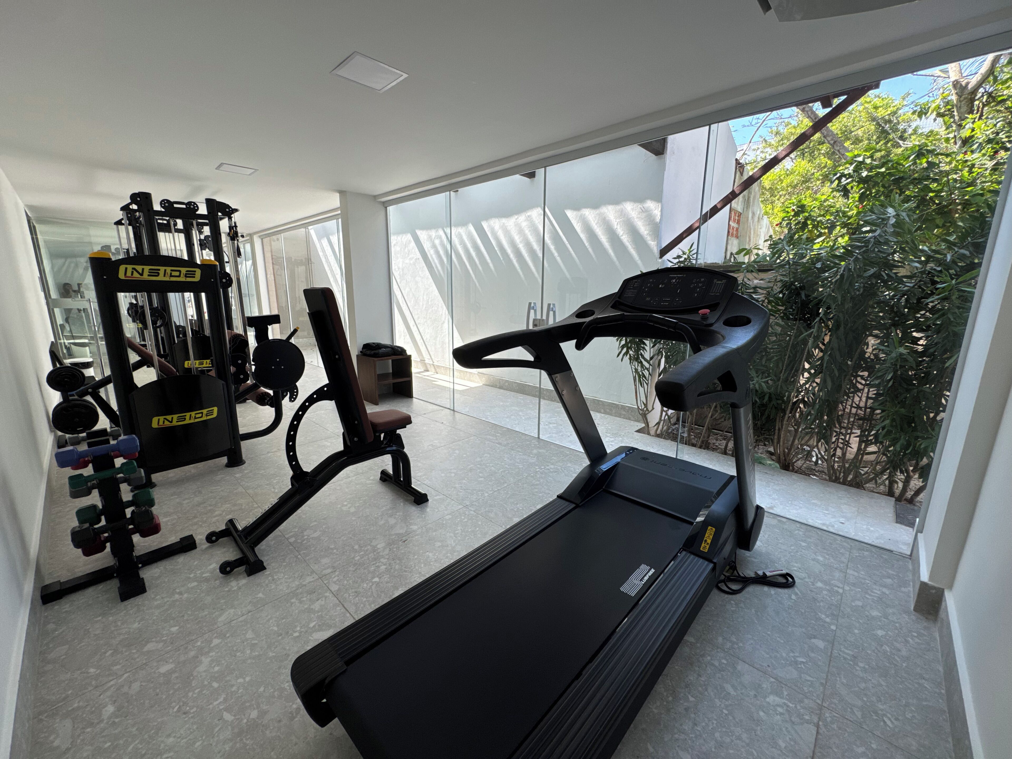 A modern gym with a treadmill, weight machines, and a bench.