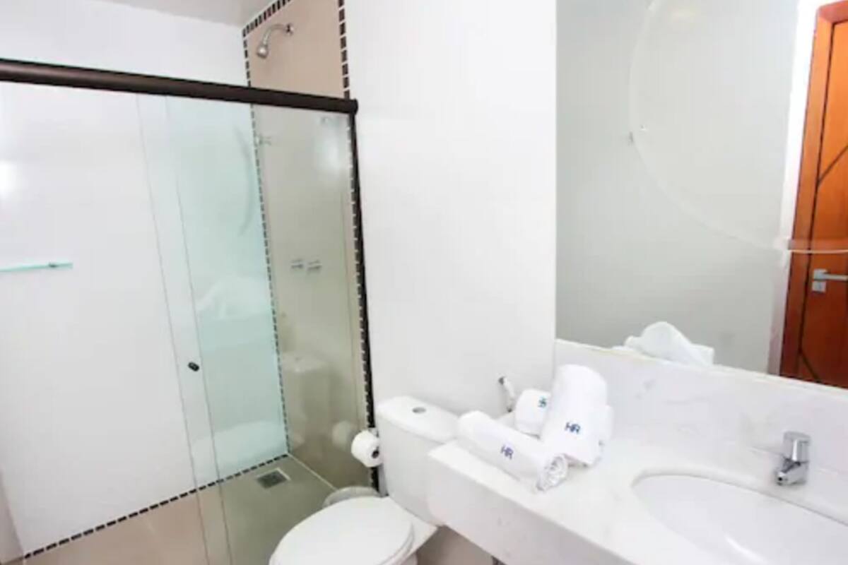 A bathroom with a glass shower enclosure, a toilet, a sink with toiletries, and a mirror.