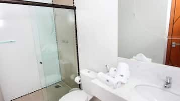 A bathroom with a glass shower enclosure, a toilet, a sink with toiletries, and a mirror.