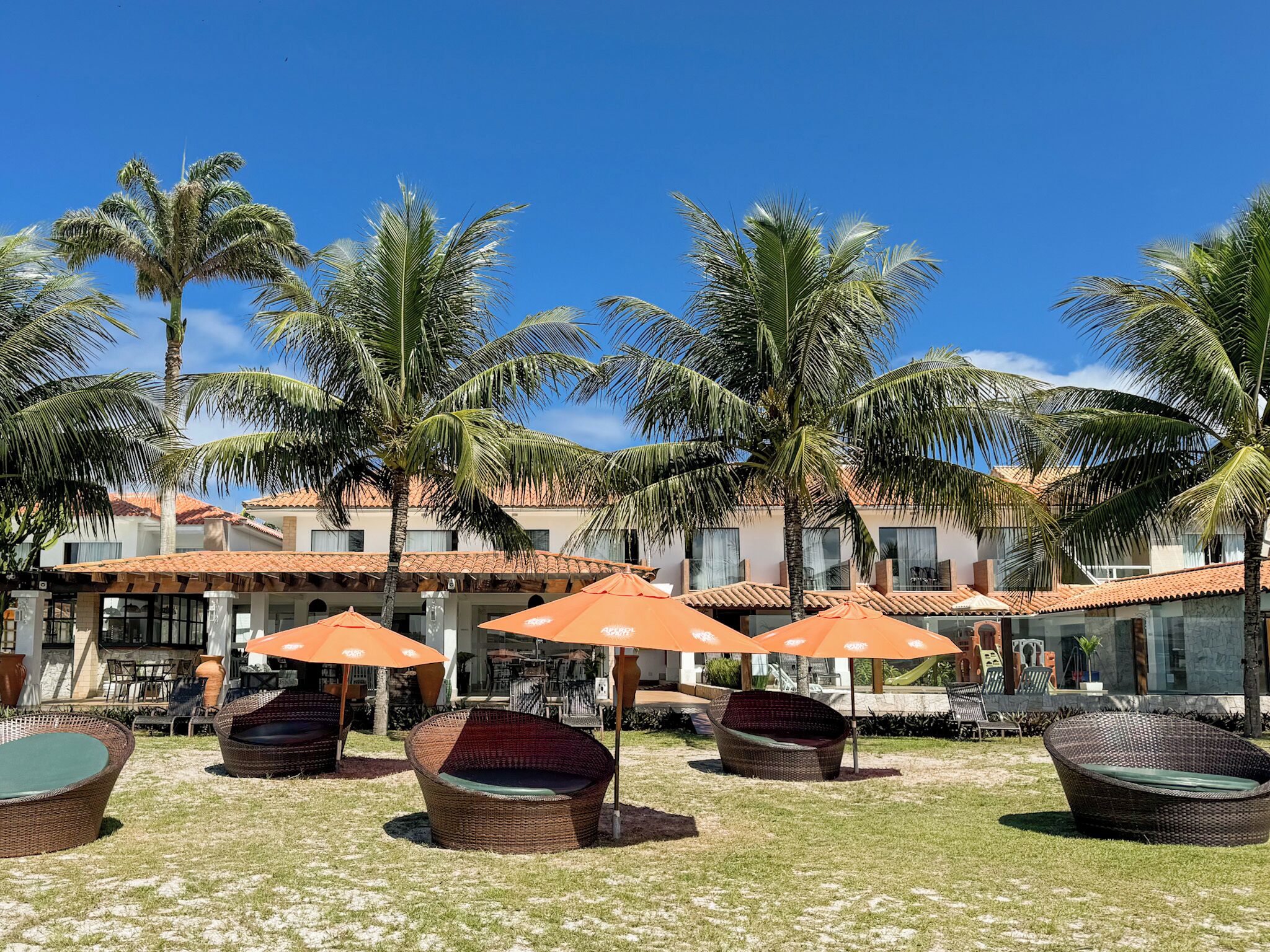A resort with outdoor seating, palm trees, and a building with a tiled roof.